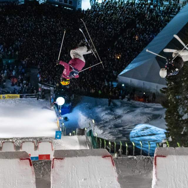 Two skiers perform aerial tricks in the dual moguls competition at night at Deer Valley in Park City, UT