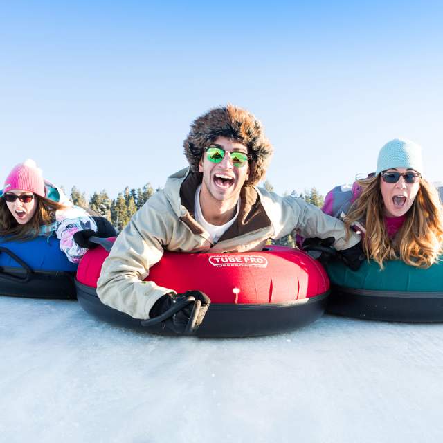 three people enjoying winter tubing