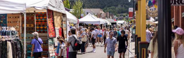 A crowd of people walk among booths at the Kimball Arts Festival on a sunny day in Park City, UT