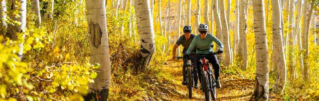 Two riders smile as they ride their bike through fall leaves on a trail near Park City, UT