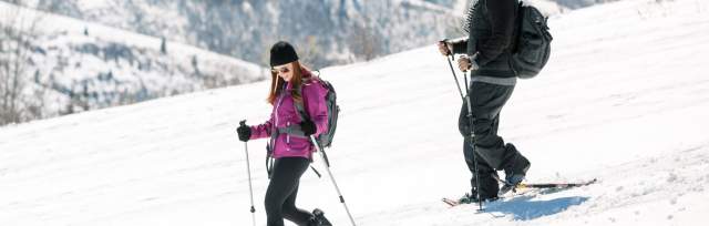 Couple snowshoeing down hill with ski resort in background