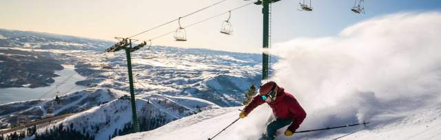 A skier carves a turn in front of a rising sun and chair lift at Deer Valley in Park City, UT