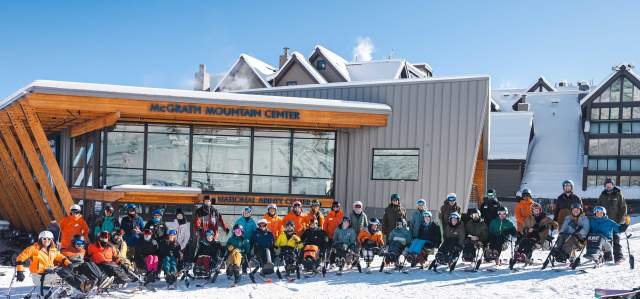 A group of adaptive athletes and instructors pose on the snow in front of the McGrath Mountain Center at Park City Mountain