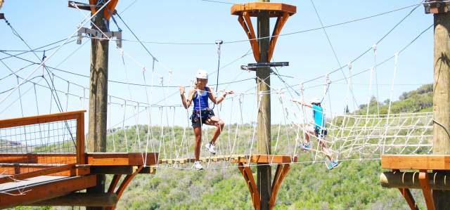 Two smiling children navigate a high ropes course on a bright summer day at the Utah Olympic Park in Park City, UT