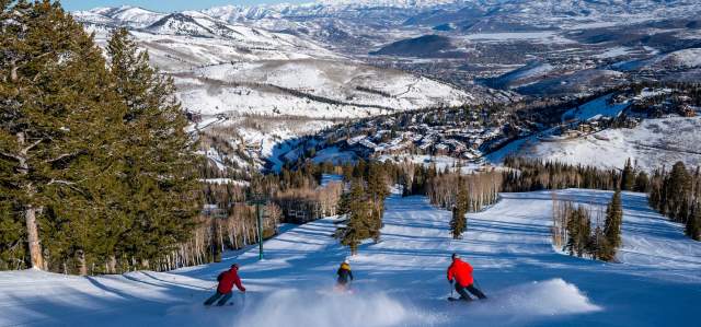 Three skiers descend a freshly groomed run on a sunny winter day at Deer Valley Resort in Park City, UT