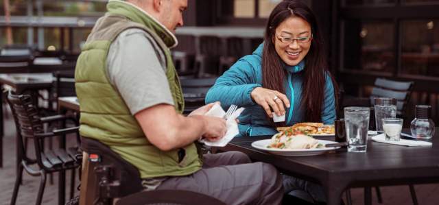 A person in a wheelchair eats a meal with another person on an outdoor deck at a restaurant in Park City, UT