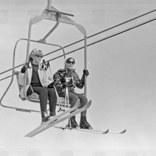 A black and white image of two women riding an old two person chairlift in Park City, UT