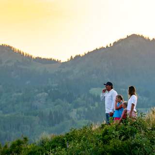 A family hiking stops at an overlook on a trail with a mountain view at sunset near Park City, UT