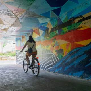 A cyclist rides a bike through a tunnel painted with a mural in front of the McPolin Barn in Park City, UT