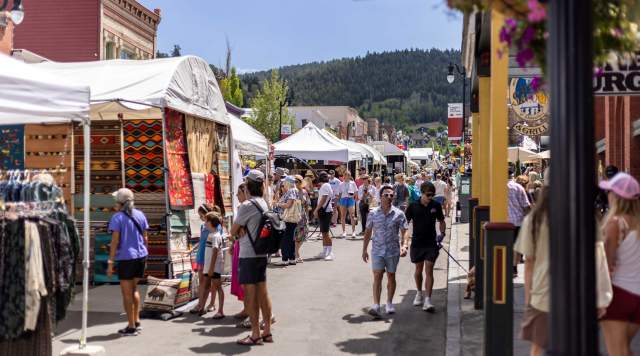 A crowd of people walk among booths at the Kimball Arts Festival on a sunny day in Park City, UT