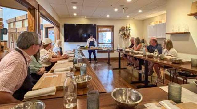 A group of people sit at long tables while listening to a chef at the Deer Valley Creative Academy in Park City, UT