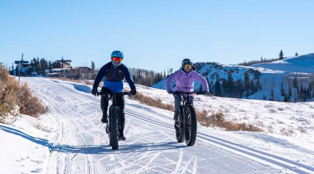 A couple rides fat bikes on a groomed trail on a sunny day near Park City, UT