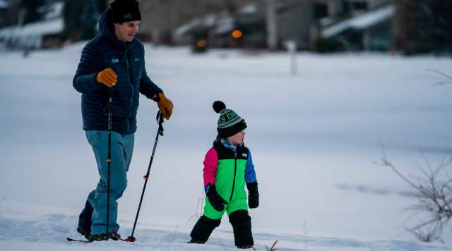 A father and son snowshoe across an open field in Park City, UT