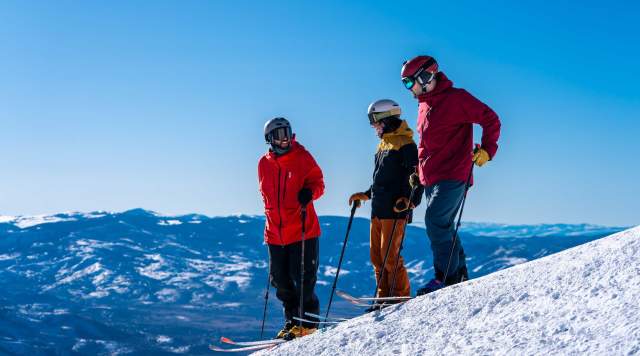 Three skiers talk at the top of a ski run on a bluebird day at Deer Valley in Park City, UT