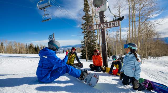 Clients and an instructor discuss snowboarding technique on a ski run underneath an art installation at Park City Mountain