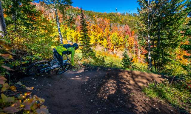 A mountain biker rounds a berm turn on a trail surrounded by fall leaves in Park City, UT