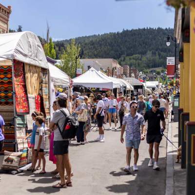 A crowd of people walk among booths at the Kimball Arts Festival on a sunny day in Park City, UT