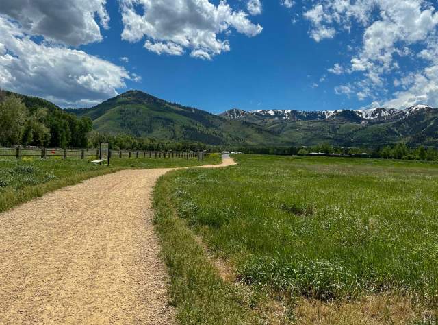 A gravel path in a meadow surrounded by green grass and trees in Park City, UT