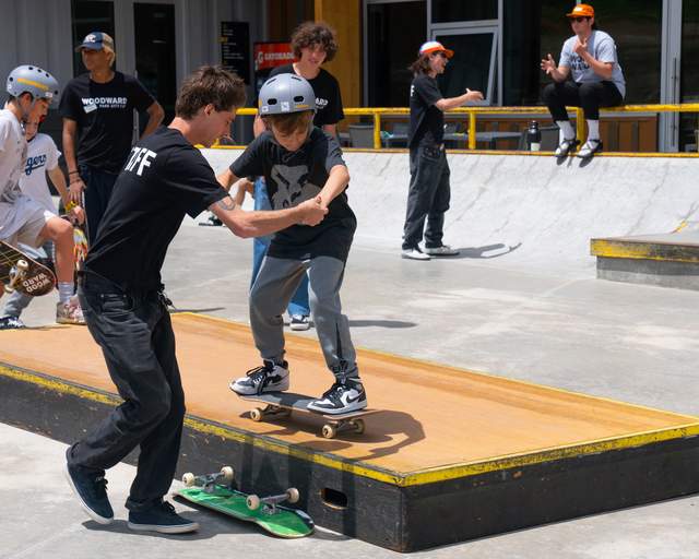 An instructor helps a child skateboard across a grind box at Woodward in Park City, UT