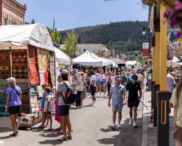 A crowd of people walk among booths at the Kimball Arts Festival on a sunny day in Park City, UT