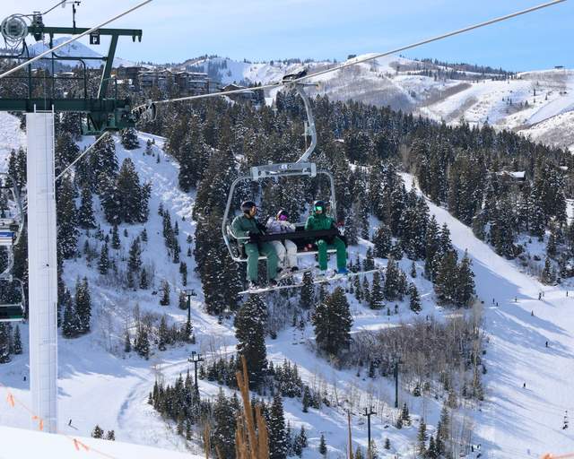 Skiers ride a chairlift with a ski instructor on a sunny day at Deer Valley Resort in Park City, UT