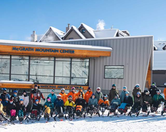 A group of adaptive athletes and instructors pose on the snow in front of the McGrath Mountain Center at Park City Mountain