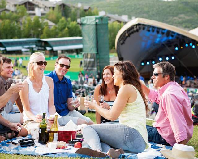 A group of friends and family enjoy wine and hors d'oeuvres at an outdoor concert on a green lawn at Deer Valley in Park City, UT