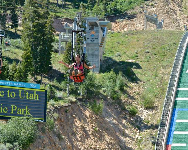 Two women ride a zip line on a summer day over the Nordic ski jumps at the Utah Olympic in Park City, UT