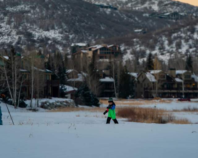A father and son snowshoe across a snowy field in front of lodging and hotels in Park City, UT