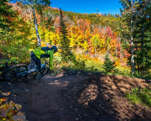 A mountain biker rounds a berm turn on a trail surrounded by fall leaves in Park City, UT