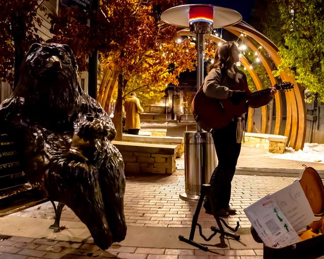 A woman plays a guitar next to a bronze statue of "Franz" the bear on Main Street, Park City, UT