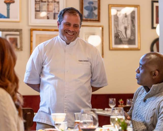 A group of friends sitting at a table laugh and smile with a chef at Le Depot in Park City, UT