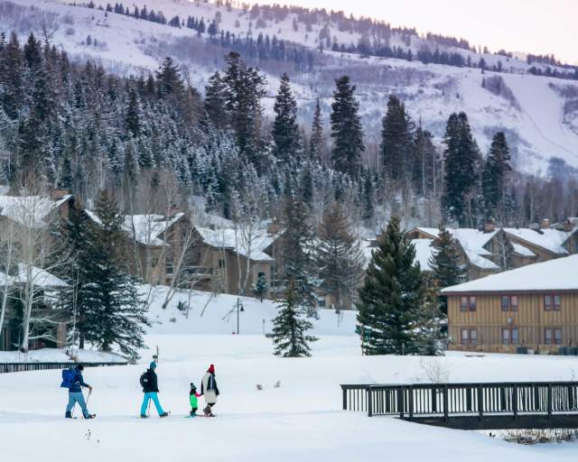A family of four and a guide snowshoe towards a wooden bridge at sunset in Park City, UT
