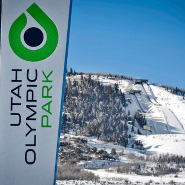 A sign for the Utah Olympic Park in front of Nordic ski jumps covered in snow in Park City, UT