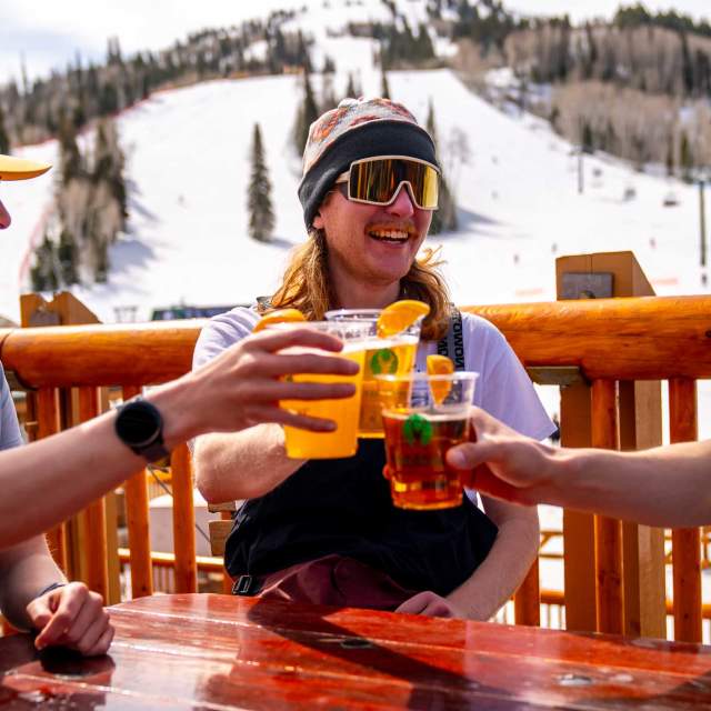 Three skiers cheers beers on a slopeside deck at Deer Valley in Park City, UT