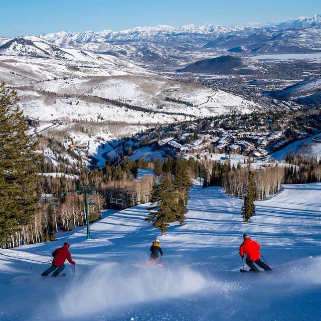Three skiers descend a freshly groomed run on a sunny winter day at Deer Valley Resort in Park City, UT