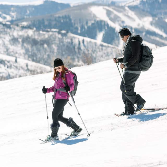 Couple snowshoeing down hill with ski resort in background