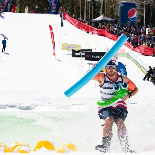 A skier in a costume skims across a pond on skis in front of a crowd at Park City Mountain in Park City, UT