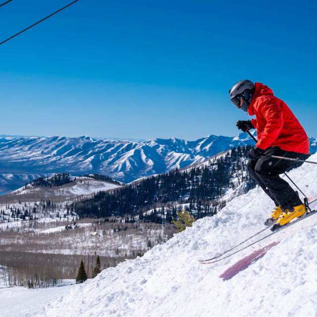 A skier drops into a ski run while skiers riding a chairlift look on in Park City, UT