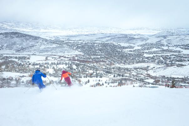 Two people skiing at Park City Mountain with a view of the town in the background