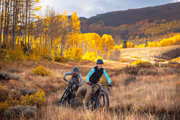 Two mountain bikers ride across an alpine meadow surrounded by colorful fall leaves near Park City, UT