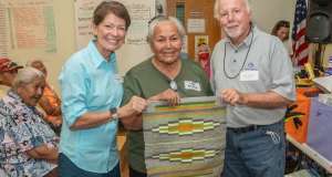 Three people holding up a navajo rug