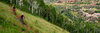 Two mountain bikers ride a trail surrounded by green grass overlooking Deer Valley in Park City, UT