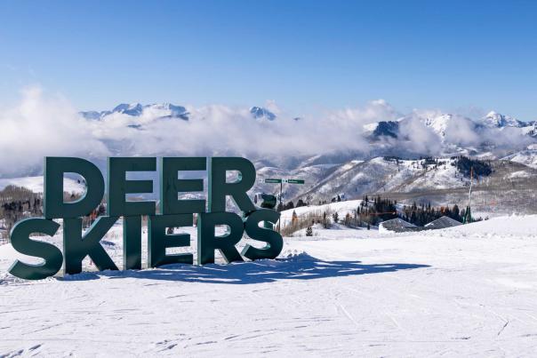 The Deer Skiers green sign at the top of a groomed ski run on a sunny day with mountain and light fog in the background at Deer Valley in Park City, UT