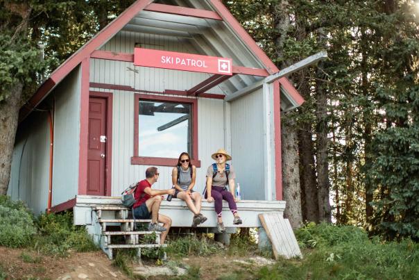 Three friends rest and laugh at a ski patrol shack on a summer hike in Park City, UT