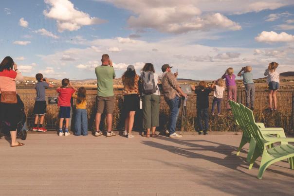 A large group of adults and young kids look out over the Swaner Nature Preserve on windy day in Park City, UT