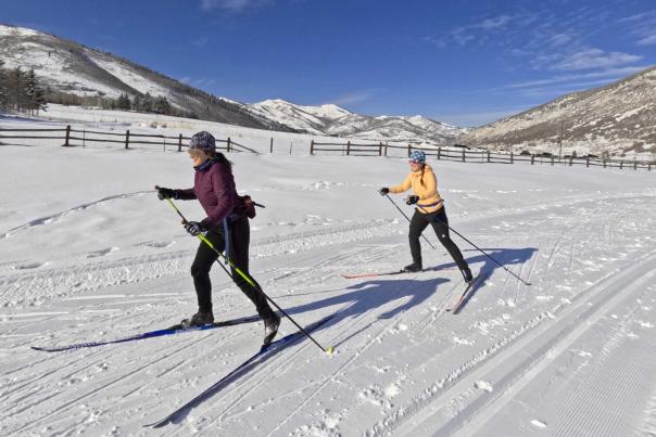 Two Nordic skiers skate along a groomed trail and cattle fence in Park City, UT