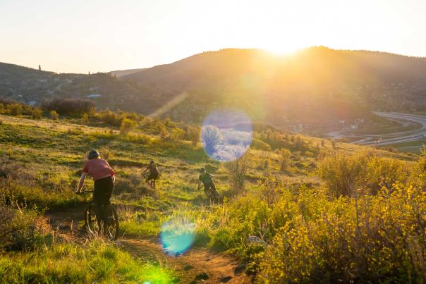 Three mountain bikers descend a trail at sunset in Park City, UT