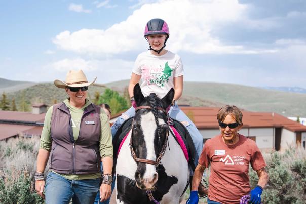 An adaptive horseback rider poses for a picture with two instructors at the NAC Ranch in Park City, UT