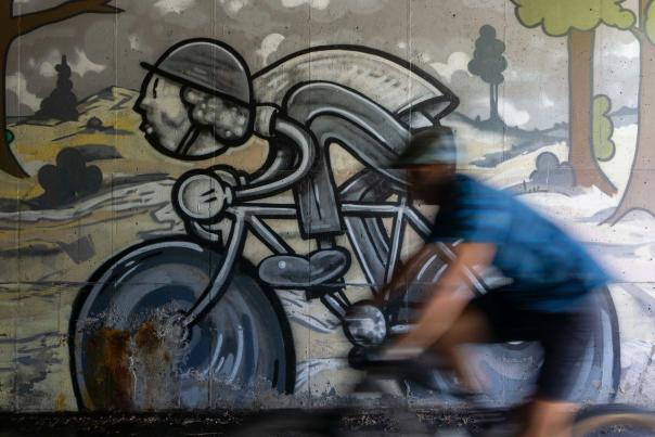 A cyclist rides by a cartoon figure riding a bike in a mural in a tunner on a path near Deer Valley Drive in Park City